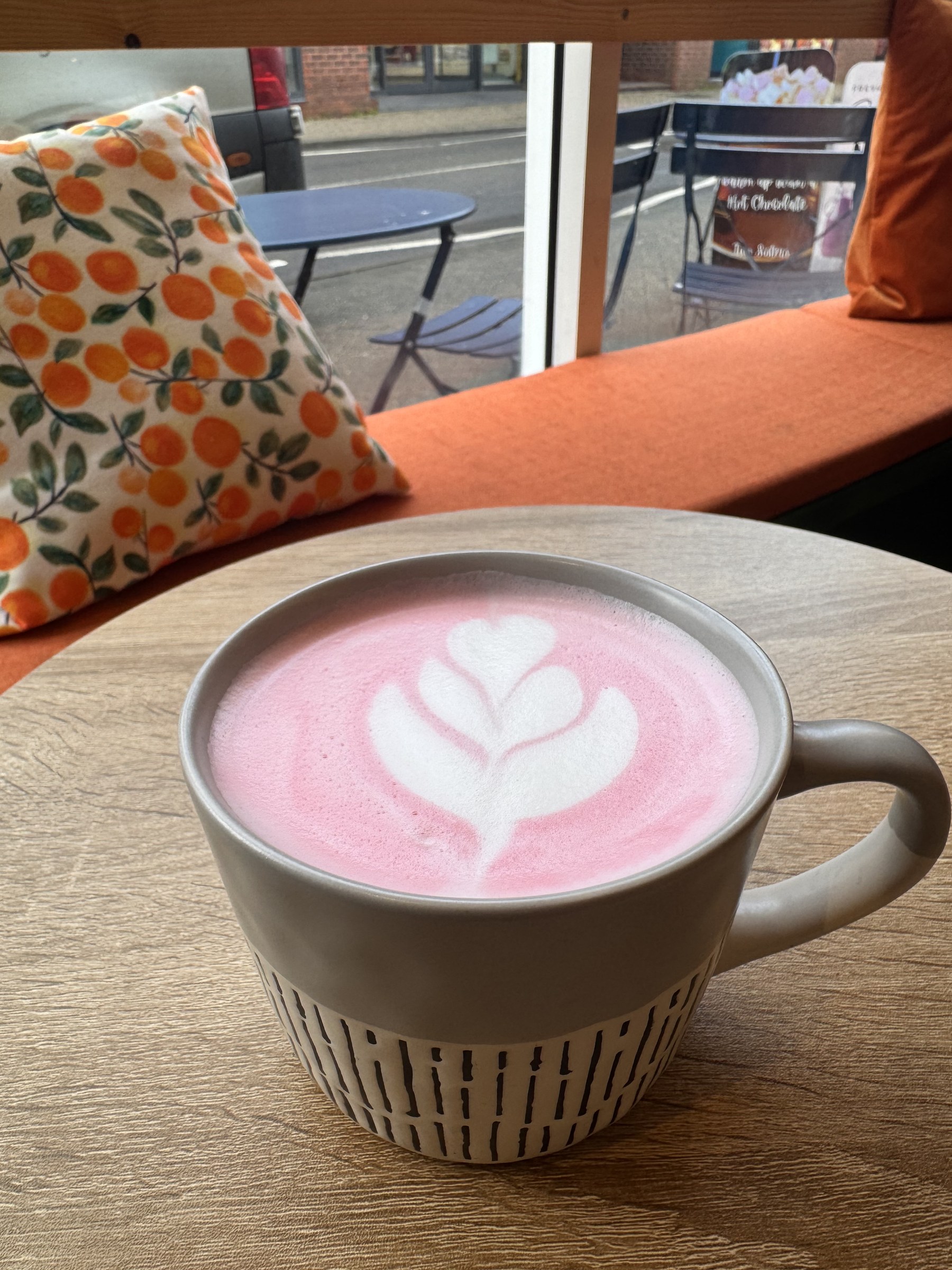 A pink beetroot latte on the table by the orange cushions
