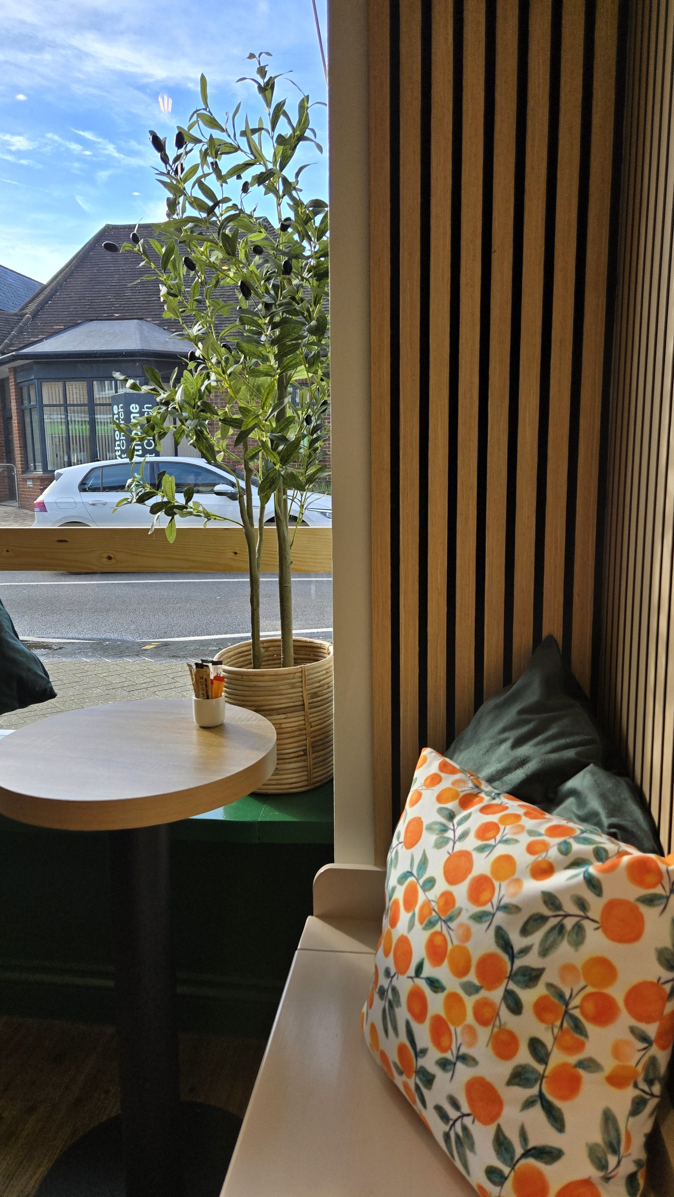 Inside Two Sisters: tan chairs, slatted wood wall and the orange cushions in the afternoon sun
